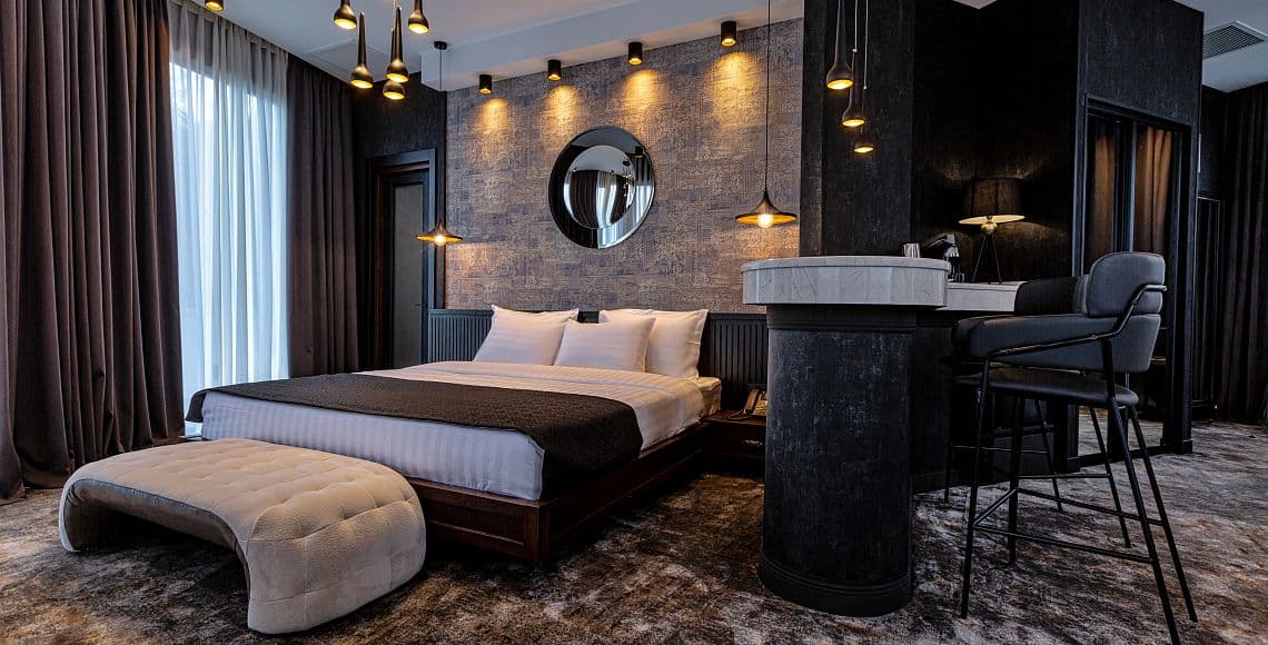 A suite bedroom with a double bed, round wall mirror and a marble bar counter with high stools