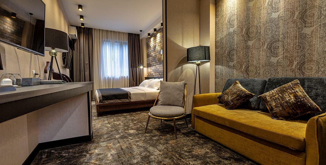 A junior suite with a double bed, mustard sofa and patterned feature wall