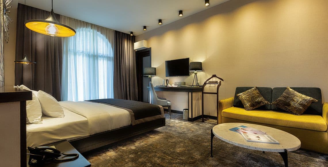 A suite with a double bed, arched window and a mustard sofa