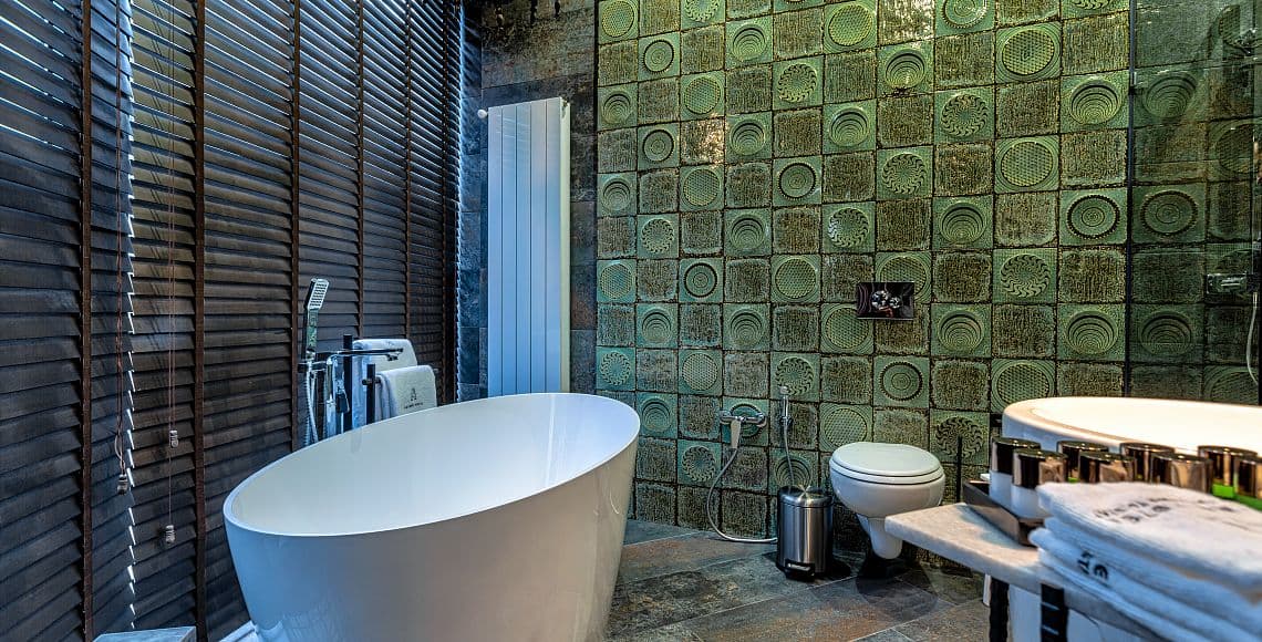 An en-suite bathroom with a freestanding oval bath against green patterned tiling