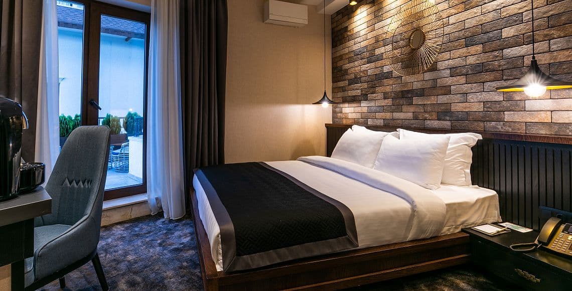 A double room with a brick feature wall, sunburst mirror and balcony doors